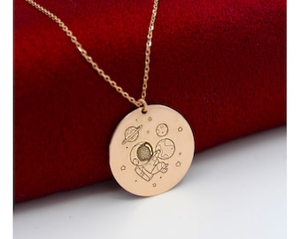 May include: A gold necklace with a round pendant featuring an astronaut floating in space with planets and stars.