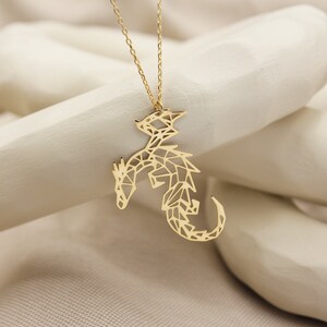 May include: A gold necklace with a geometric dragon pendant. The dragon is made of a delicate, intricate design.