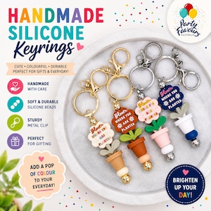 May include: Silicone keyrings with a plant theme. Each keyring has a flower-shaped tag with the text "Bloom where you are planted." The keyrings have a sturdy metal clip and come in various colours, including white, brown, pink, and blue. Ideal for gifts.
