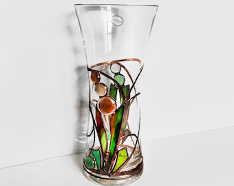 May include: A clear glass vase with a copper wire design and stained glass accents in shades of green, brown, and orange. The vase is decorated with a floral motif.