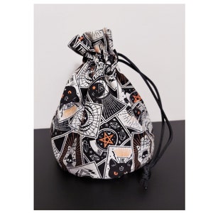 May include: A drawstring pouch with a black and white pattern featuring tarot card illustrations, black cats, and celestial designs. The pouch has a black drawstring closure.
