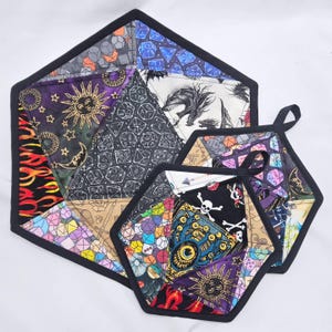 May include: A set of three quilted, hexagonal pot holders and a matching trivet. The fabric features a patchwork design with dice, dragons, skulls, and suns in various colors. Each piece has a black border and the pot holders have black loops.