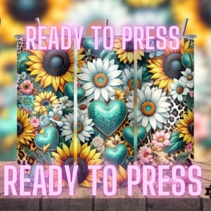 May include: Three sublimation tumblers with a floral design featuring sunflowers, daisies, and turquoise hearts. The tumblers are ready to be pressed with a design.