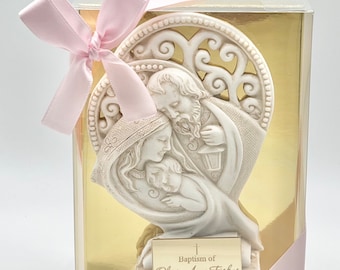 Peut inclure: Figurines en céramique blanche de la Sainte Famille dans un cadre en forme de cœur. La figurine est dans une boîte transparente avec un ruban rose et un fond doré. La boîte a une plaque dorée avec le texte "Baptism of Olivia Anna Fiskus".