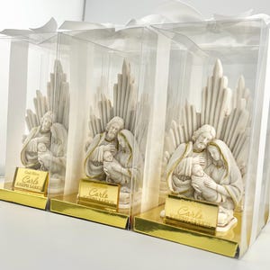 May include: Three white ceramic figurines of the Holy Family in a clear plastic box with a gold label that reads "God Bless Carlo Joseph Sarkis".