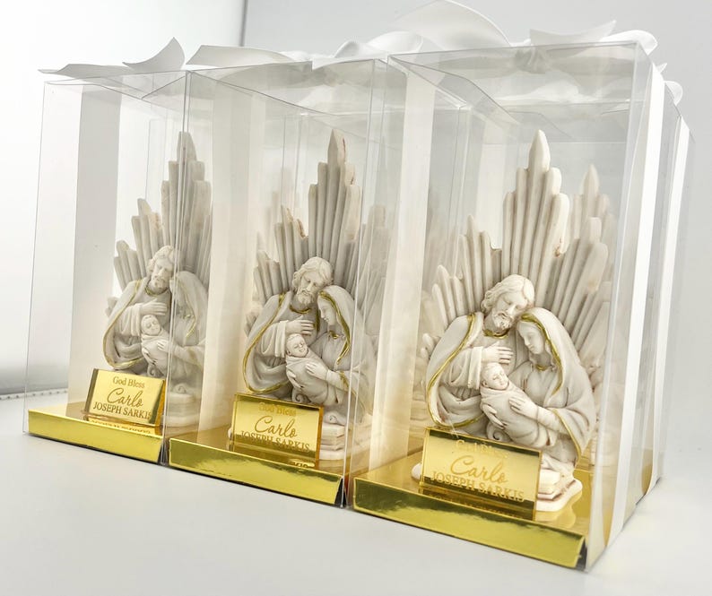 May include: Three white ceramic figurines of the Holy Family in a clear plastic box with a gold label that reads "God Bless Carlo Joseph Sarkis".