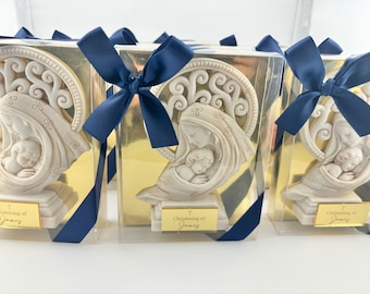 Peut inclure: Un ensemble de figurines en céramique blanche de la Vierge Marie et de l'enfant Jésus dans une boîte en plastique transparente avec un fond doré et un ruban bleu. La boîte porte une étiquette dorée sur laquelle est inscrit "Baptême de James".