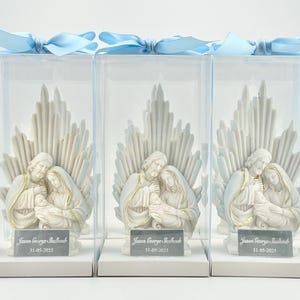 May include: Three white ceramic figurines of the Holy Family in a clear plastic box with a blue ribbon. The figurines are of Mary, Joseph, and baby Jesus. The boxes have a white label with the text "Jason George Ballard 31-05-2023".