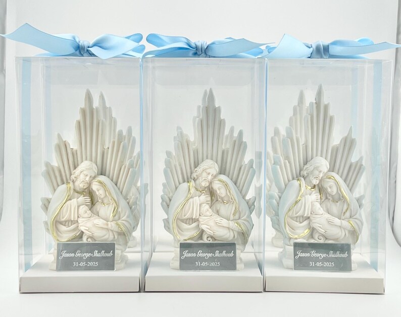 May include: Three white ceramic figurines of the Holy Family in a clear plastic box with a blue ribbon. The figurines are of Mary, Joseph, and baby Jesus. The boxes have a white label with the text "Jason George Ballard 31-05-2023".