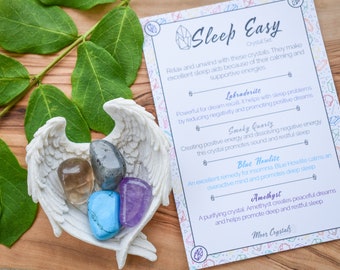 Puede incluir: Un conjunto de cinco cristales en un soporte blanco con forma de ala de ángel. Los cristales son Labradorita, Cuarzo Ahumado, Howlita Azul y Amatista. Los cristales son para dormir y relajarse. La tarjeta dice "Sleep Easy Crystal Set".