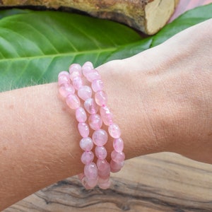 May include: A bracelet made of pink rose quartz beads. The bracelet is made of multiple strands of beads and is worn on a person's wrist.