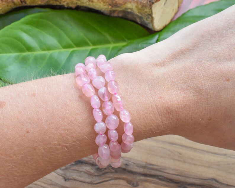 May include: A bracelet made of pink rose quartz beads. The bracelet is made of multiple strands of beads and is worn on a person's wrist.