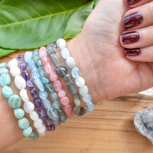 Op de afbeelding: Een stapel van tien armbanden gemaakt van verschillende halfedelstenen, waaronder amethist, aquamarijn, aventurijn en rozenkwarts. De armbanden zijn allemaal gemaakt van gladde, ovale kralen.