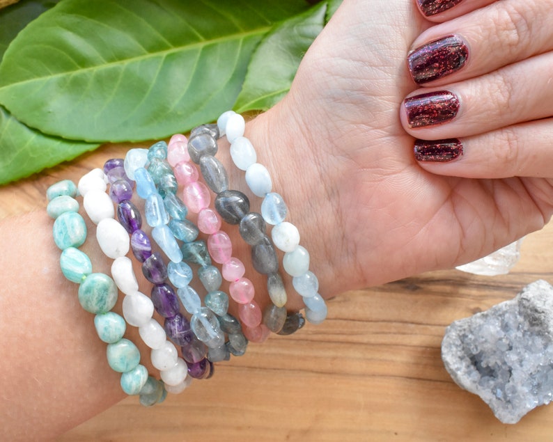 Op de afbeelding: Een stapel van tien armbanden gemaakt van verschillende halfedelstenen, waaronder amethist, aquamarijn, aventurijn en rozenkwarts. De armbanden zijn allemaal gemaakt van gladde, ovale kralen.