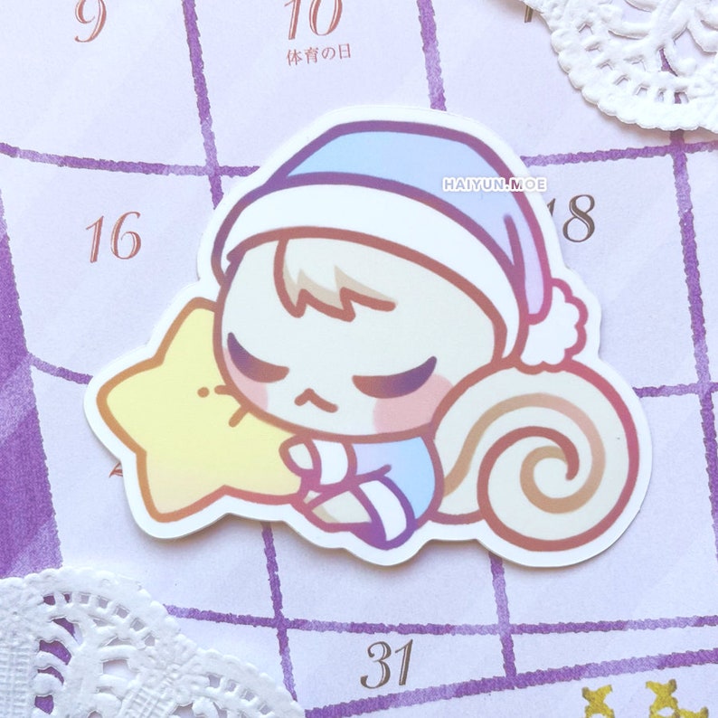 May include: A sticker of a cartoon animal wearing a blue and white sleep cap, holding a yellow star and curled up with a brown tail. The sticker is on a purple and white calendar with the text "HAI YUN MOE" and the number "18" visible.
