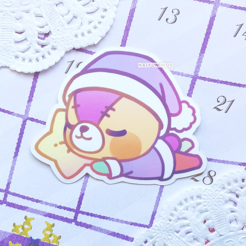 May include: A sticker of a purple and brown bear wearing a purple and white sleep cap and holding a yellow star. The bear is sleeping and has a stitched scar on its face. The sticker is on a white background with purple lines.