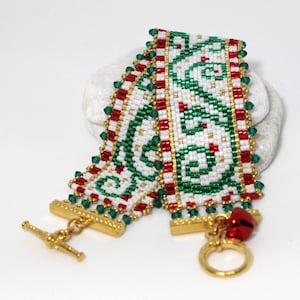 May include: A beaded bracelet with a green, white, and red pattern. The bracelet has a gold clasp and a small bell charm.
