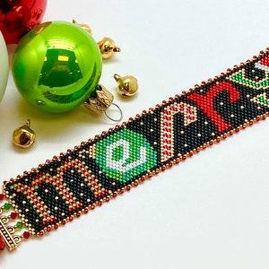 May include: A beaded bracelet with the word "Merry" spelled out in red, green, and white beads on a black background. The bracelet has gold-colored clasps and bells.