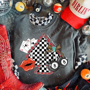 May include: A gray sweatshirt with a graphic featuring playing cards, a checkered design, and two 8-ball pool balls. A red cowboy boot, a baseball cap with "DARLIN" text, and various billiard balls are also visible.
