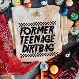 K&ouml;nnte beinhalten: Cremefarbenes T-Shirt mit dem schwarzen Text "FORMER TEENAGE DIRT BAG" und einem Schachbrettmuster. Umgeben von roten Cowboy-Stiefeln, Discokugeln und Billardkugeln.