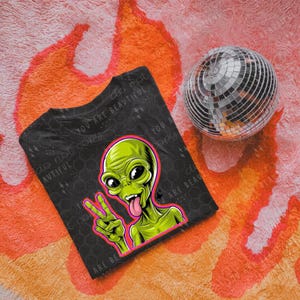 May include: Black t-shirt with a green alien graphic wearing a pink peace sign. The alien has a green tongue sticking out. The text "do not copy you are beautiful" is printed on the shirt.
