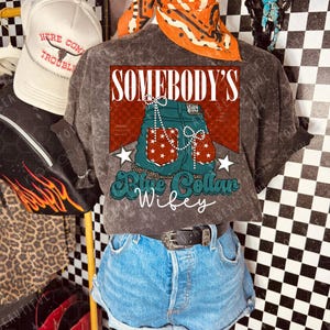 May include: A display featuring a grey t-shirt with a graphic of blue jean shorts and the text "SOMEBODY'S Blue Collar Wifey." The shirt is paired with denim shorts and a black belt. An orange bandana and a white trucker hat are also visible.