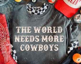 May include: A gray sweatshirt with the text "THE WORLD NEEDS MORE COWBOYS" is displayed with a red cowboy boot, a white and red baseball cap, and billiard balls. The sweatshirt has a checkered collar.