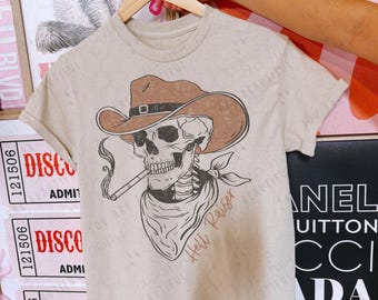 May include: A beige t-shirt with a graphic of a skeleton wearing a cowboy hat and smoking a cigarette. The text "Hell Raiser" is written below the skeleton.