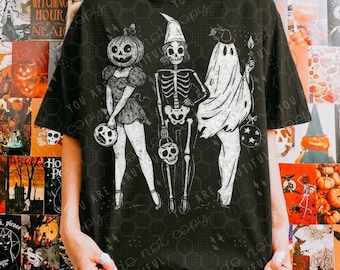 Może przedstawiać: Czarny t-shirt z białym nadrukiem przedstawiającym trzy postacie z Halloween: kobietę z dyniową głową, szkielet i ducha. Każda postać trzyma latarnię w kształcie czaszki. Koszulka ma okrągły dekolt i krótkie rękawy. Na koszulce wydrukowano napis "YOU ARE BEAUTIFUL".