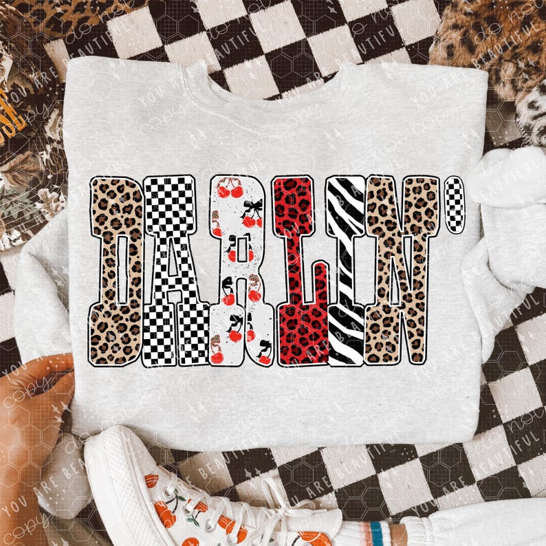 May include: A light gray sweatshirt with the word "DARLIN'" in a bold, multi-patterned design. The letters feature leopard print, checkerboard, cherries, and zebra stripes. White sneakers with cherry graphics are visible.