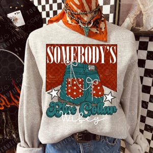 May include: A light grey sweatshirt with a graphic design of blue jeans with red and white stars, the words "SOMEBODY'S" and "Blue Collar Wifey". The sweatshirt is worn with denim shorts and a brown belt.