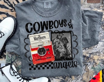 May include: A gray t-shirt with the words "Cowboys & Angels" in black. The shirt features a graphic of a red and white camera and a black and white photo. White boots and camouflage pants are also visible.