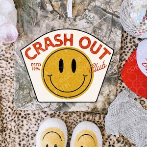May include: A camouflage print t-shirt with a "Crash Out Club" graphic featuring a yellow smiley face. White slippers with smiley faces are at the bottom. A disco ball and a red and white hat are also visible.