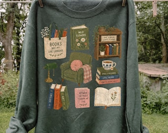 Könnte beinhalten: Ein dunkelgrüner Rundhals-Pullover mit einem Grafikdruck, der eine Tragetasche mit dem Text "BOOKS ARE MY LOVE LANGUAGE", ein Bücherregal, einen grünen Sessel, einen Bücherstapel, eine Teetasse und ein offenes Buch mit Blumen zeigt.