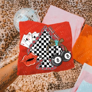 May include: Red graphic tee featuring a black and white checkered spade, a pair of eight balls, playing cards, and red lips. The text "FEELIN' LUCKY" is also visible. The design is set against a leopard print background.
