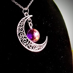 May include: A silver crescent moon pendant necklace with a purple and gold gemstone hanging from the bottom.
