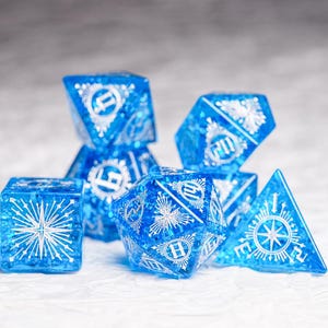 Op de afbeelding: Een set blauwe dobbelstenen met witte sneeuwvlokontwerpen en een stervormig patroon. De dobbelstenen zijn gemaakt van helder plastic met een glinsterende afwerking.