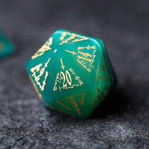 Könnte beinhalten: Ein grüner zwanzigseitiger Würfel mit goldener Beschriftung. Der Würfel hat ein einzigartiges Design mit einem Schwert und der Zahl 20 auf einer Seite.