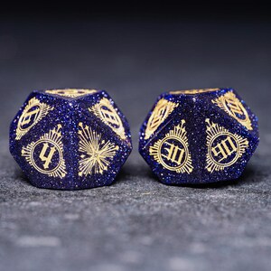 Op de afbeelding: Twee blauwe en gouden dobbelstenen met een glinsterende afwerking. De dobbelstenen zijn genummerd 4 en 10.