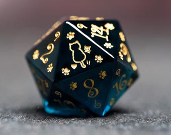 May include: A dark blue, multi-sided dice with gold numbers and paw print designs. The dice has a cat silhouette on one side.