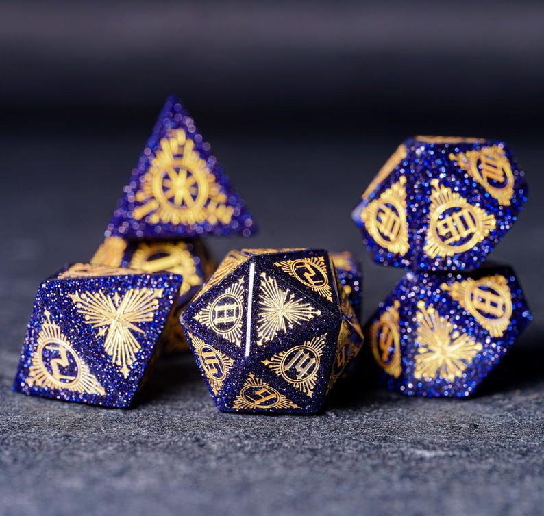 Op de afbeelding: Een set van zes blauwe en gouden dobbelstenen met een stervormig ontwerp. De dobbelstenen zijn gemaakt van een glinsterend materiaal en hebben een uniek, ingewikkeld ontwerp.