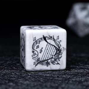 May include: A white, marble-textured die with black musical note and harp illustrations. The die features a detailed design of a harp, musical notes, and floral accents. The die is set against a dark background.