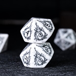 May include: Two white and gray marbled D20 dice stacked on top of each other. Each die features black musical instrument and floral designs. The numbers 4 and 20 are visible on the dice. Other dice are blurred in the background.