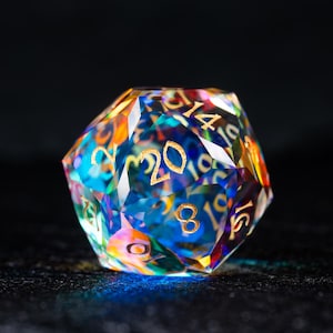 May include: A multi-faceted, iridescent, crystal d20 dice with gold numbers. The dice is a twenty-sided die used in tabletop role-playing games.