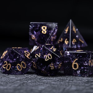 May include: A set of six polyhedral dice for tabletop games. The dice are a deep purple with a speckled, galaxy-like pattern and gold numbering. Includes a D4, D6, D8, D10, D12, and D20.