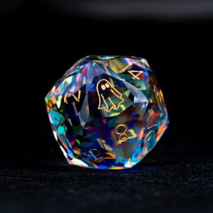May include: A multi-faceted, iridescent polyhedral die featuring a translucent, rainbow-colored finish. The surface is engraved with gold-colored numbers and a small ghost icon on one of the faces, reflecting light with a prismatic effect.