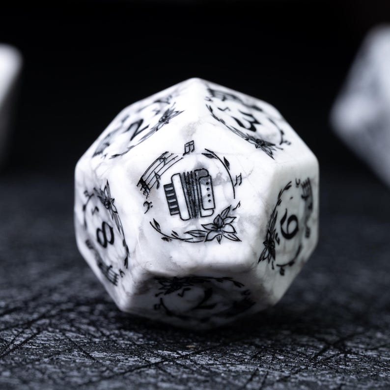 May include: A white and gray marbled D20 die with black etched details. The die features numbers and an illustration of an accordion surrounded by musical notes and floral elements. The die is set against a dark background.