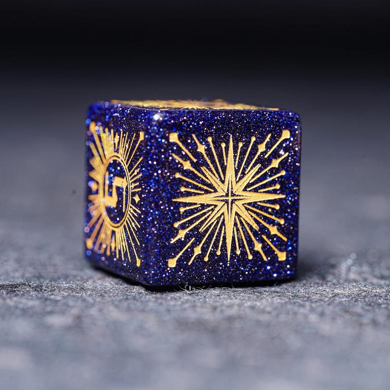 Op de afbeelding: Een blauwe en gouden dobbelsteen met een stervormig ontwerp. De dobbelsteen is gemaakt van een glinsterend materiaal.