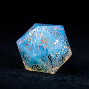 May include: A twenty-sided die with a translucent, pale blue, opalescent finish. The die features engraved numbers in a metallic copper colour, including a prominent number 20 at the top, along with numbers 8, 14, and 16 clearly visible on the facets.