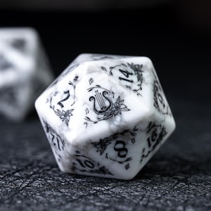 May include: A white and gray marbled D20 die with black floral and musical note designs. The numbers are in black. The die is a polyhedral shape, used for tabletop role-playing games.